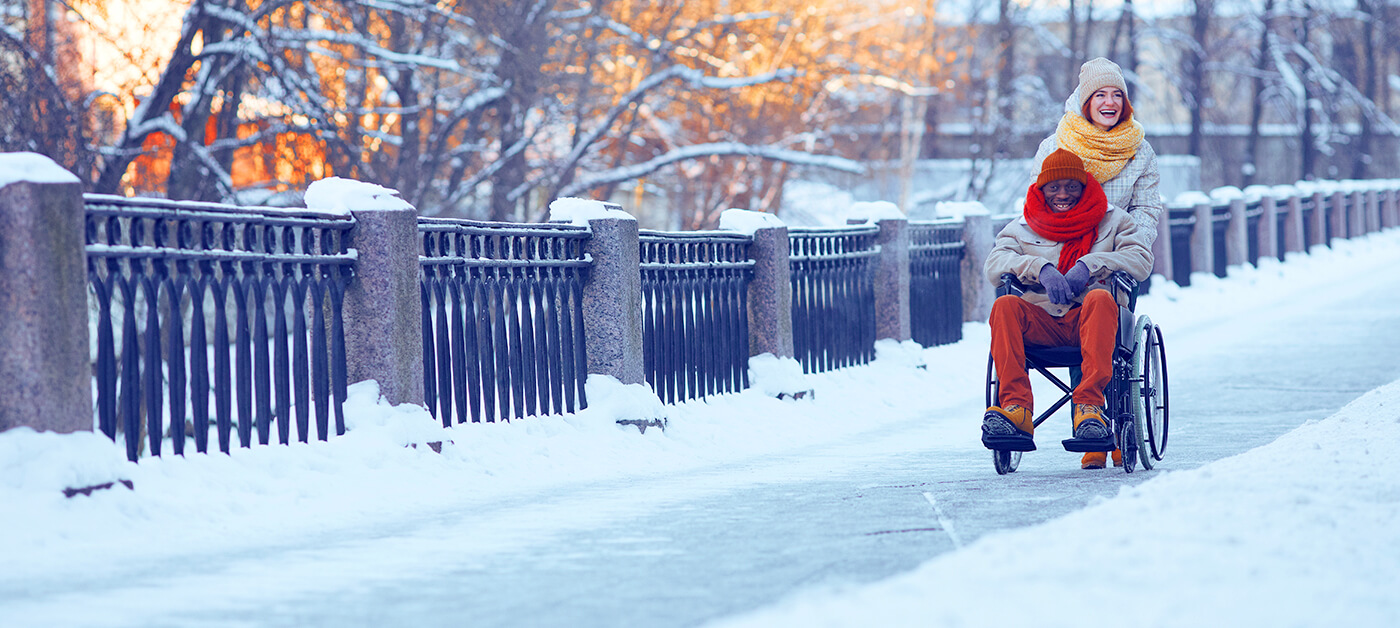 A young woman pushes her friend in a wheelchair so he can enjoy the winter season.