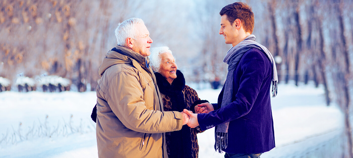 An elderly couple warmly thank their young neighbor by shaking his hand.