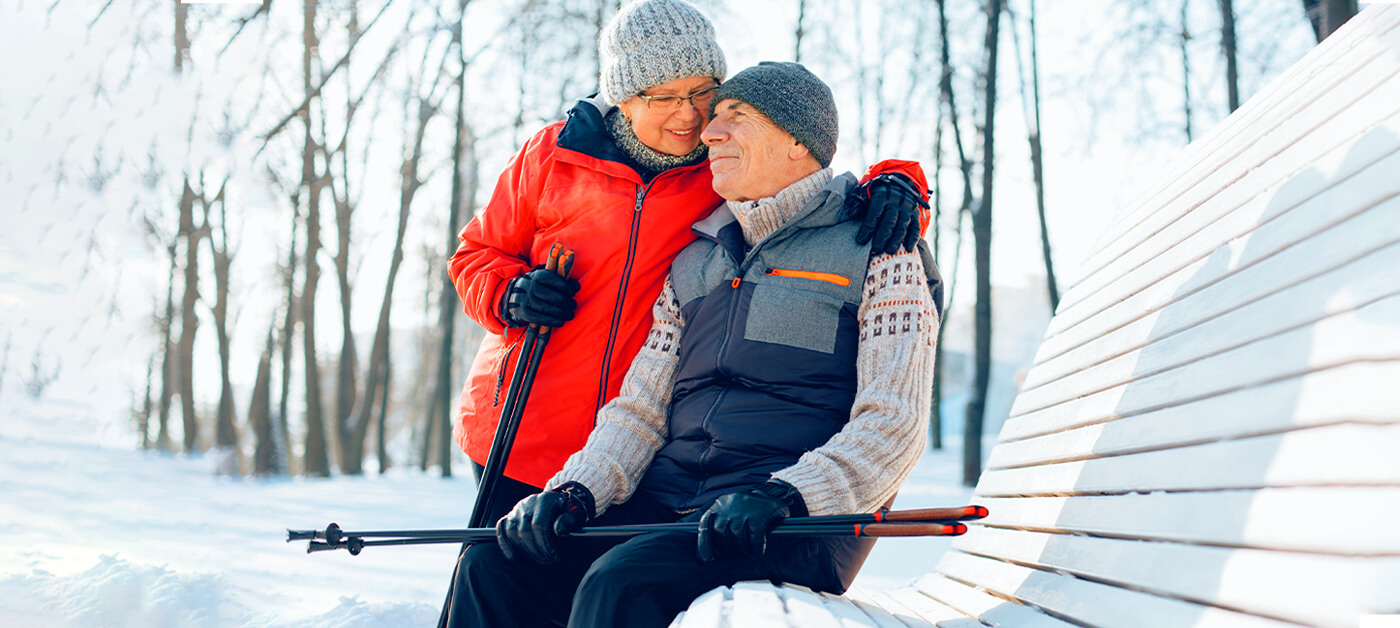An elderly couple takes advantage of a sunny winter day to go for a walk in the park with their walking sticks.
