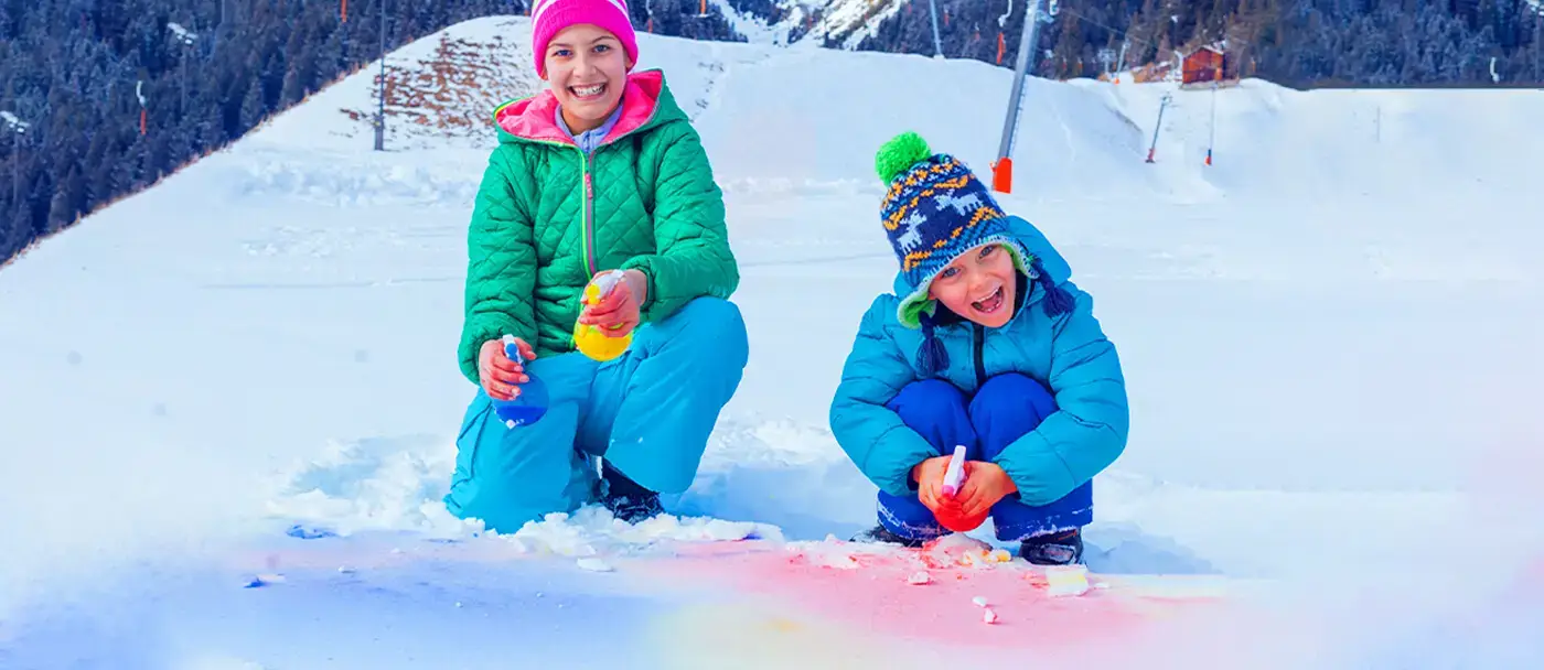 A mother and her son are drawing on the snow with homemade paint bottles.